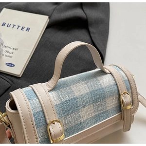 Close-up of blue plaid canvas handbag with cream leather trim and gold metal buckles