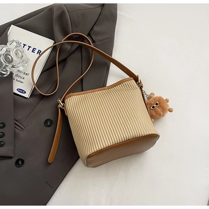 Macro detail of beige pleated bucket bag with brown leather trim and fuzzy monster charm