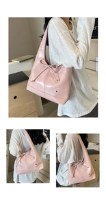 Detail of pink glossy shoulder bag featuring a drawstring bow and small heart metal plaque