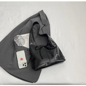 Detail of black glossy leather hobo bag with adjustable bow and heart charm on gray suit