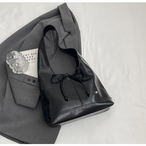 Close-up of black glossy shoulder bag with drawstring bow and silver heart pendant