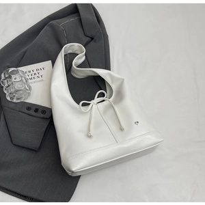 Flat lay of a white leather tote bag with bow detail and heart charm on a grey suit