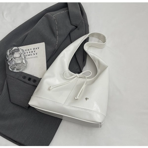 Detailed view of white patent leather hobo bag with a delicate bow and silver heart charm