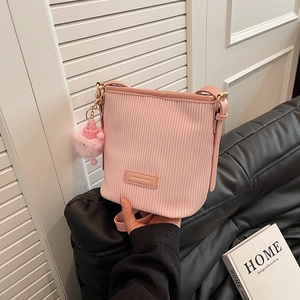Pink corduroy bucket bag with fashion label and pom-pom keychain on a shoulder strap