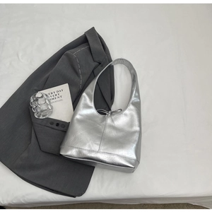 Detailed top view of silver hobo bag with pleated texture on a grey suit jacket