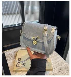 Close-up of metallic silver saddle bag featuring a rabbit ear shaped gold twist lock buckle