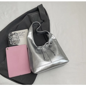 Close-up of silver metallic tote bag with bow detail and heart charm on white background