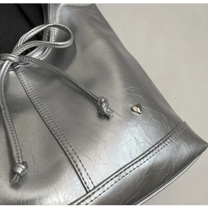 Macro view of silver bucket bag with pleated texture and heart-shaped metal stud