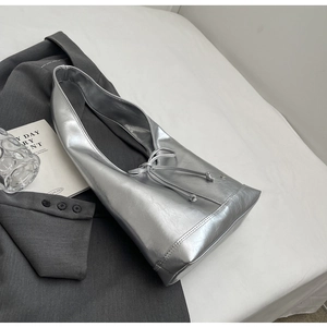 Macro detail of silver metallic tote bag with drawstring bow on grey blazer