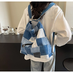 Detail of blue patchwork denim backpack showing wide straps and metallic zip pockets