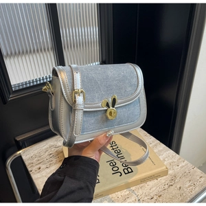 Detail of denim saddle bag featuring a gold rabbit clasp and silver metallic trim