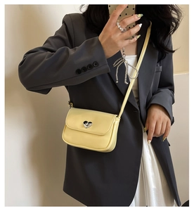 Detail of yellow leather crossbody bag with silver heart-shaped clasp worn with a blazer