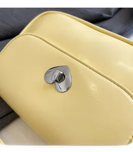 Close-up of a yellow square bag featuring a silver heart-shaped metal twist lock