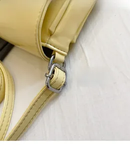 Detail of adjustable silver buckle and stitching on a light yellow leather crossbody bag