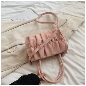 Detailed view of the light pink pleated cloud bag on a textured blazer and magazine
