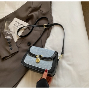 Detail of blue denim saddle bag featuring a golden rabbit-shaped twist lock buckle
