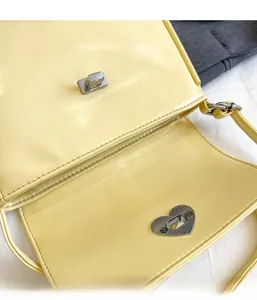 Close-up of heart-shaped metal twist lock on a yellow glossy faux leather crossbody bag
