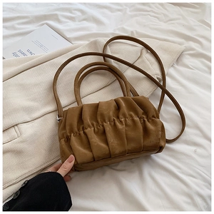 Detailed view of brown ruched cloud bag with cylinder handle on white bedding