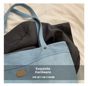 Detail of light blue denim tote bag with metal rivet and embossed leather logo tag