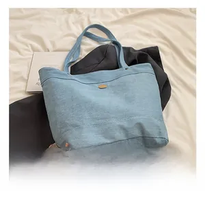 Detail showing light blue denim tote bag with metal nameplate on stylish fabric background