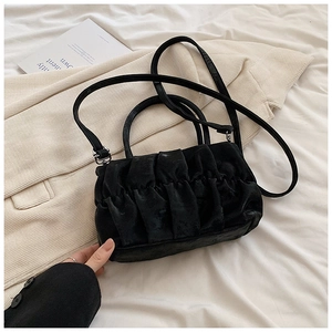 Detail of black pleated cloud bag texture on soft fabric with minimalist shoulder strap