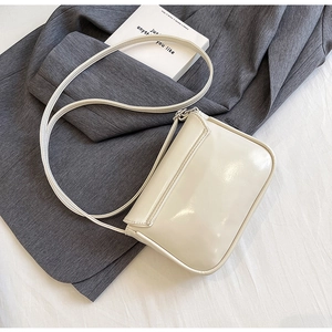 Detail view of a cream white glossy leather crossbody bag on a grey blazer background