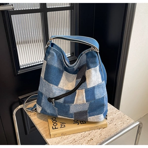 Detailed shot of patchwork blue denim tote bag with black zipper pocket on marble surface