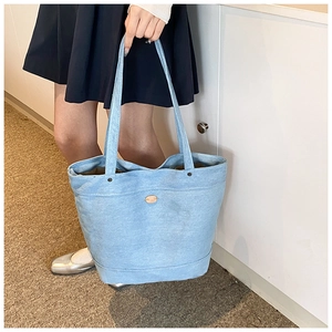 Detail of light blue denim tote bag showing metal rivet accents and textured denim fabric
