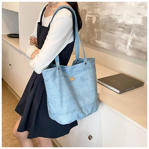 Detailed close-up of light blue denim tote bag with metal rivets and shoulder strap