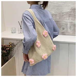 Détail d'un sac cabas en tricot beige avec fleurs au crochet porté sur l'épaule du modèle