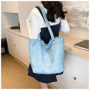 Detail of light blue denim tote bag with metal rivets and golden buckle on model shoulder