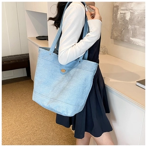 Detail of light blue denim tote bag with gold metal buckle shown on a model