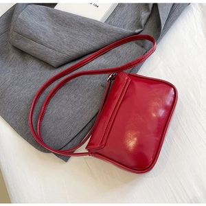 Detail of red glossy leather square bag with adjustable strap on a gray blazer