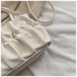 Close-up of white ruched leather cloud bag with slim strap and elegant pleats