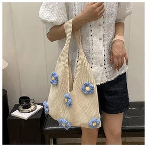 Détail du sac cabas en tricot avec des fleurs 3D bleues et jaunes sur crochet couleur crème