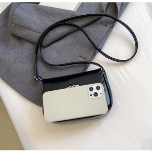 Size comparison of a black leather crossbody bag next to a smartphone on a soft surface