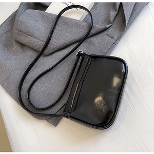 Glossy black patent leather crossbody bag resting on a gray suit jacket with a book