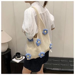 Détail d'un sac cabas en tricot beige avec des fleurs en crochet 3D bleues sur une bandoulière