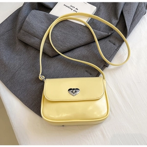 Detail of cream yellow leather handbag featuring a silver heart-shaped metal twist lock