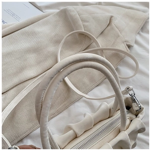 Close-up of cream pleated handbag showing wavy craft details and metal zipper closure