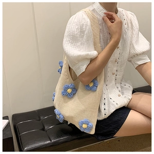 Gros plan d'un sac cabas en maille avec fleurs crochetées bleues sur texture blanche