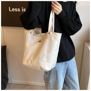 Close-up of cream leather tote bag featuring retro metal logo and stud detailing