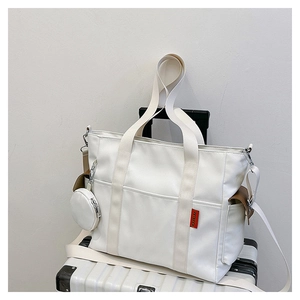 Detail of cream nylon tote bag with side pocket and round coin purse on white suitcase