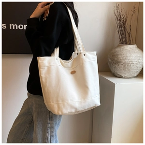 Detail of white canvas tote bag showing the oval metal logo plate on a textured surface