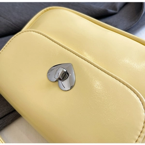 Detailed close-up of light yellow leather handbag with heart-shaped silver metal turn lock
