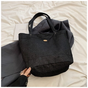 Detail view of dark grey denim tote bag with oval metal plaque and widened base