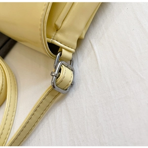 Detail of silver metal buckle and smooth faux leather texture on cream crossbody bag