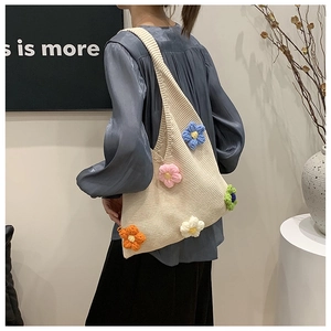 Détail d'un sac cabas en tricot crème avec fleurs 3D porté dans un décor moderne chic