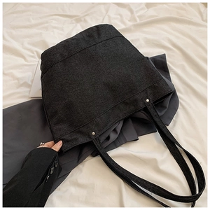 Detail of black denim tote bag showing textured fabric, stitching and silver metal rivets