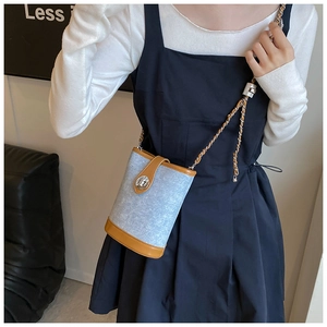 Detail view of light blue denim bucket bag with brown leather trim and metal chain strap